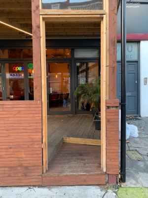 Wooden archway ahead. First step up at foot of archway followed by second step past archway. Glass door ahead.