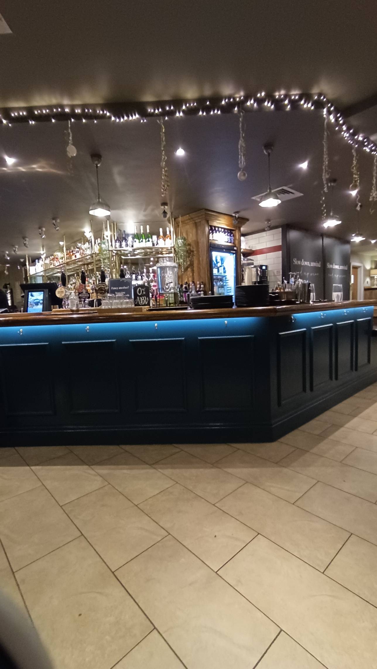 Bar immediately in front of entrance, high with no low area, lights under the bar top, brightly lit with spotlights, blue painted bar wooden top