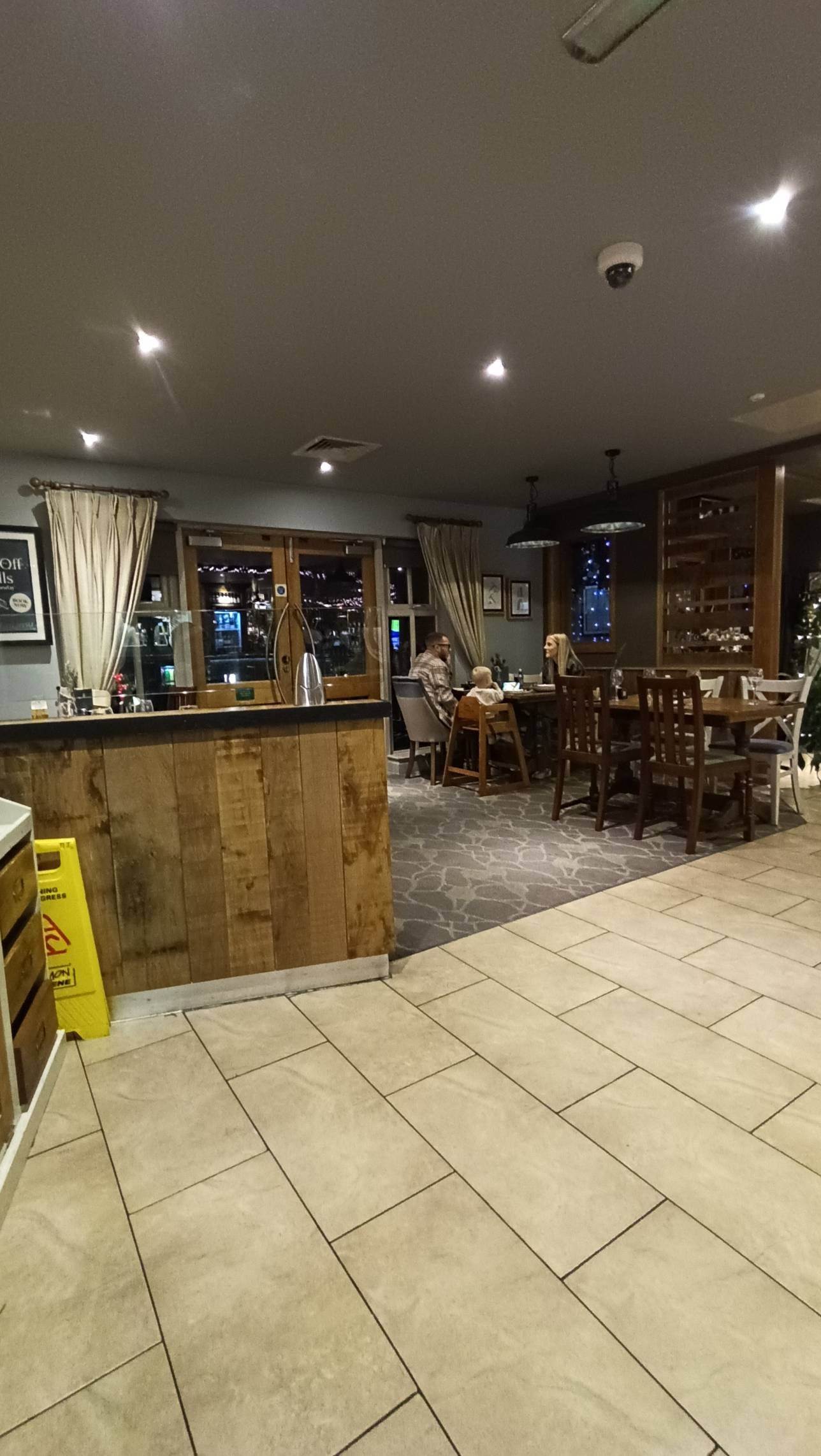 Seating area showing wooden tables seated height with chairs, carpeted flooring and tiled flooring. Glass double doors going to outside area