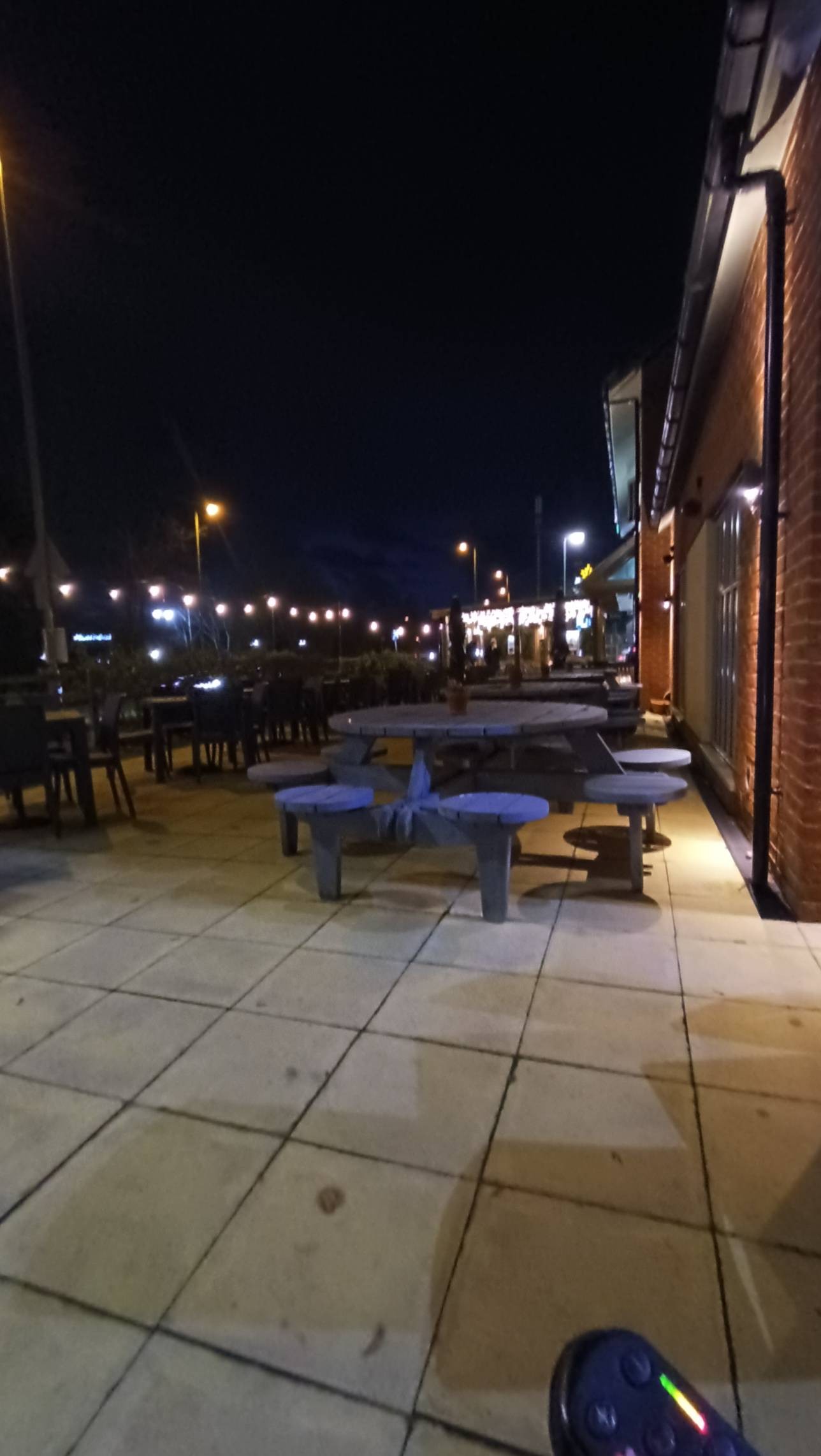 Smoking area to rear of outside area, covered area at back of photo with lighting, large amount of picnic tables, not wheelchair accessible.