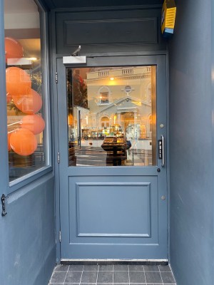 Glass door with grey wooden frame ahead. Pull silver handle on right to open.