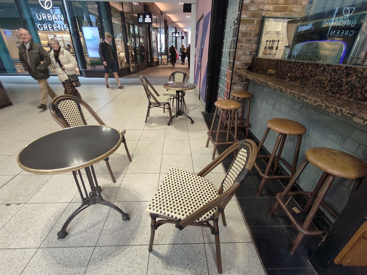 From restaurant barrier facing right. Tables and chairs ahead. High table and stools on right.