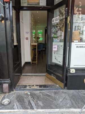 Small bump followed by step up to glass door with black frame. Pull from metal handle on left to open.