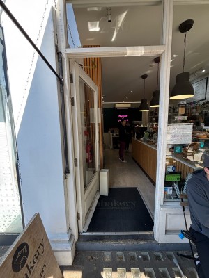 Glass door with white frame ahead. Push gold metal handle from right to open.