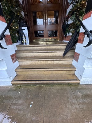 Facing steps up before main entrance. 5 concrete steps up with bannisters either side.