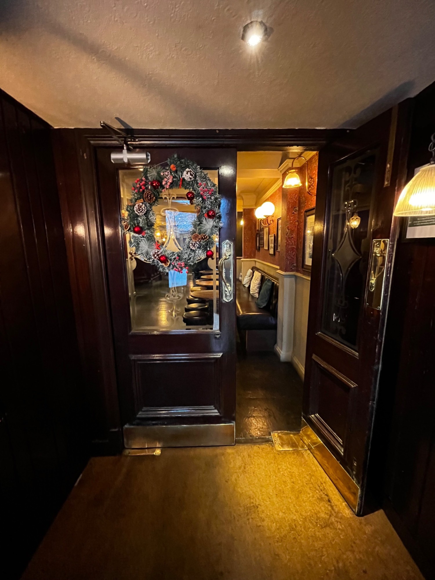 From doorway, facing straight. Glass door with brown, wooden frames ahead. Pull golden. Handles from middle to open.