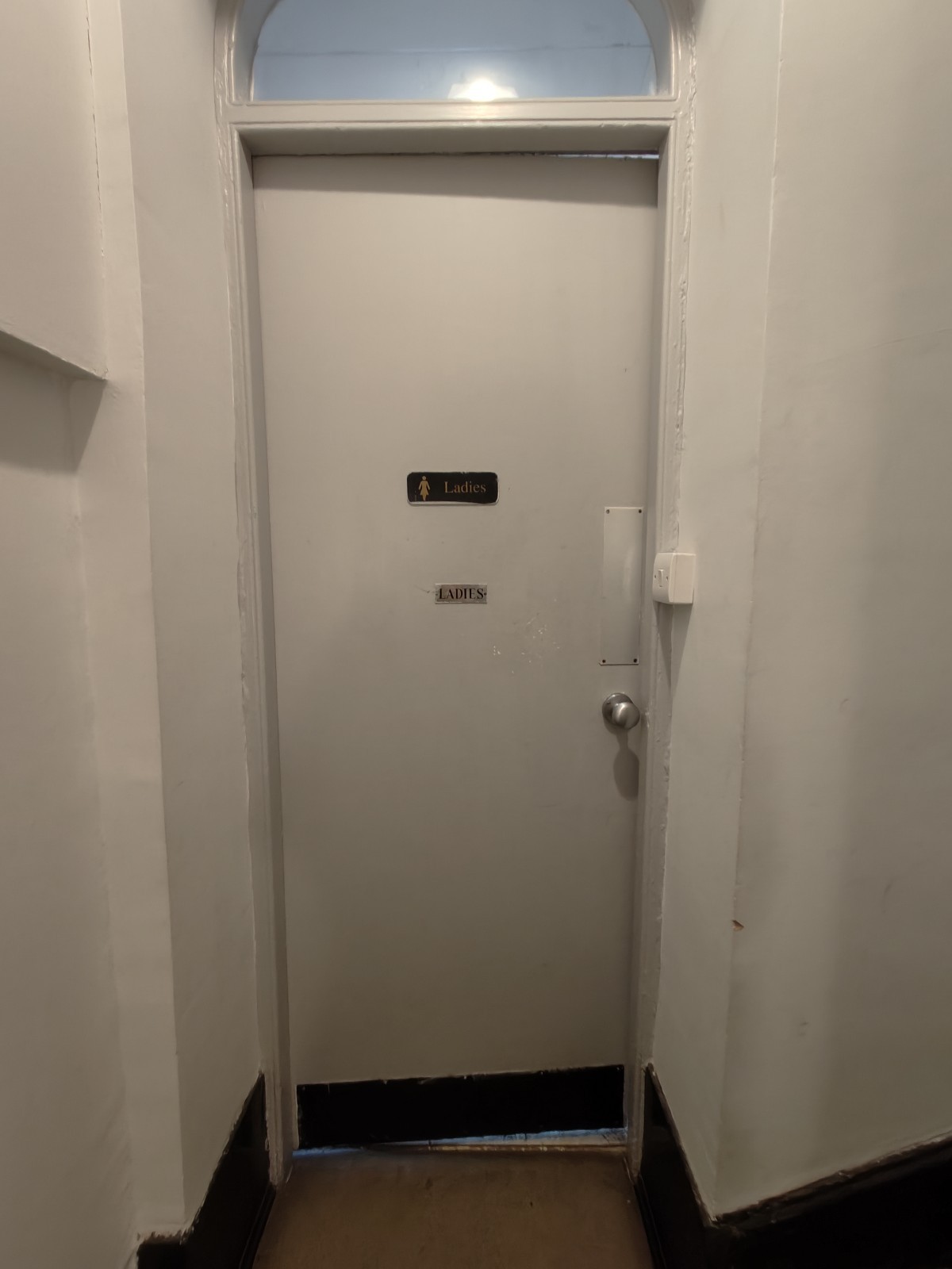 From top of stairs facing straight. Second white preceding door ahead. Push silver handle on right to open.