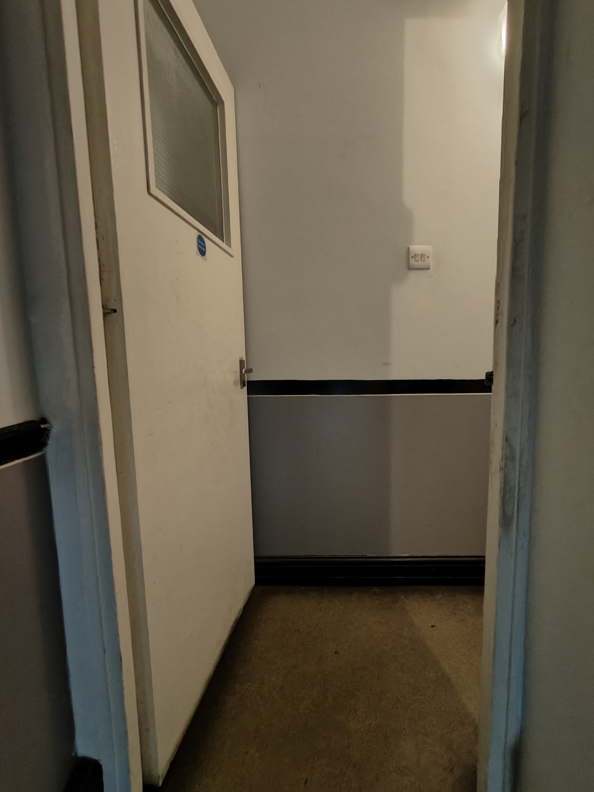 From top of stairs facing straight. First white preceding door ahead. Push silver handle on right to open.