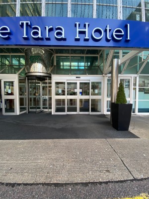 From street facing hotel entrance. Automatic doors to left and right, revolving door in centre. Facing right automatic doors. Path leads straight.