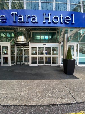 From street facing hotel entrance. Automatic doors to left and right, revolving door in centre. Facing right automatic doors. Path leads straight.