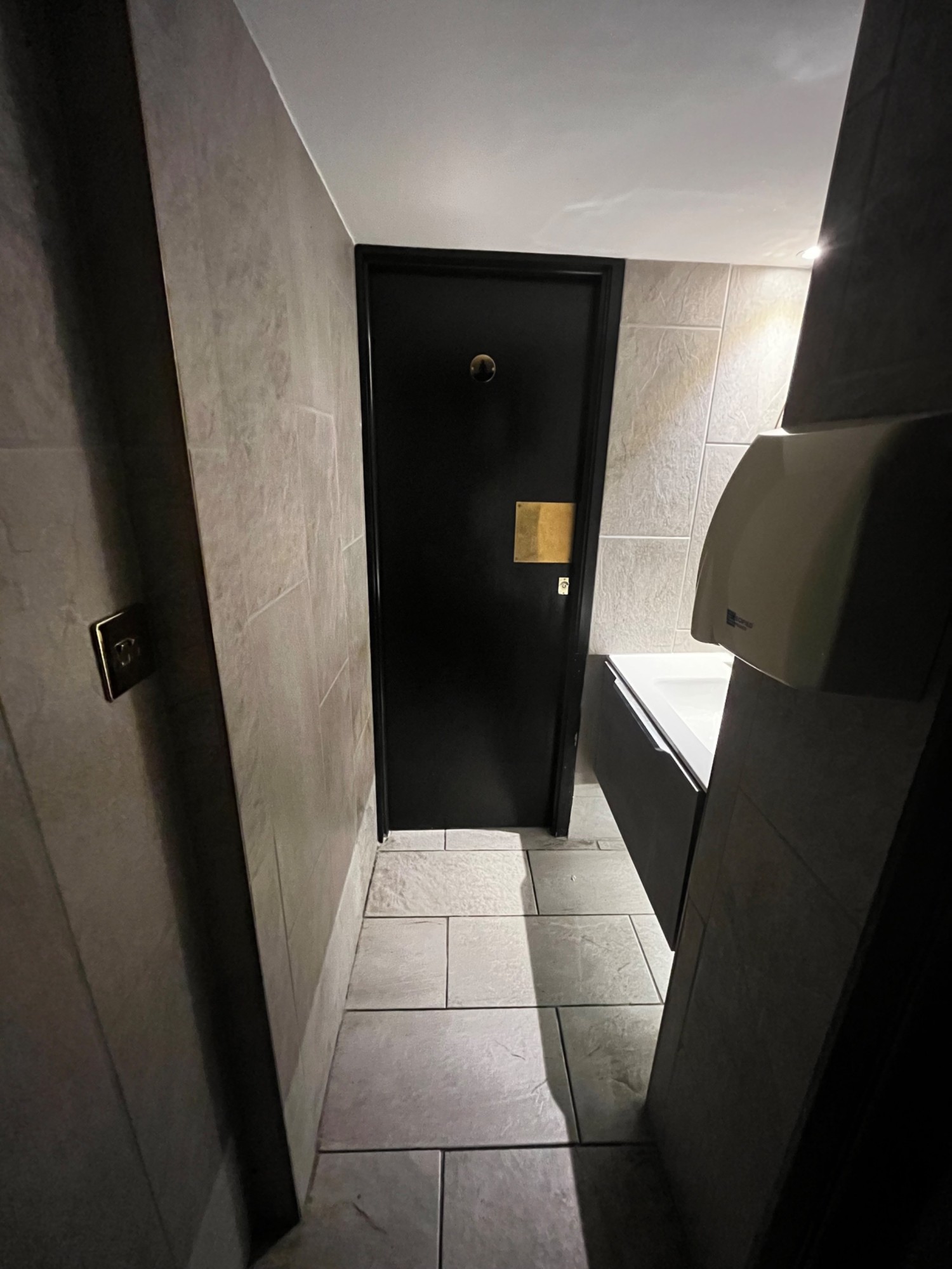 From second preceding doorway facing straight. Sink on right wall. Black wooden cubicle door on wall ahead. Push from right to open.