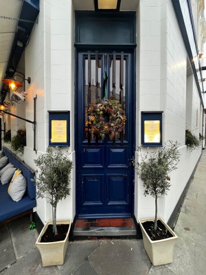 Blue and glass panelled door ahead. Push from right to open. Planters to left and right of door.