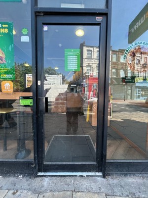 Glass door with black frame ahead. Push black handle on left to open.