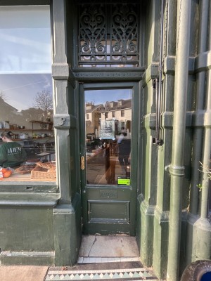 Glass door with dark green frame. Push golden handle on left to open. Small bump at threshold.