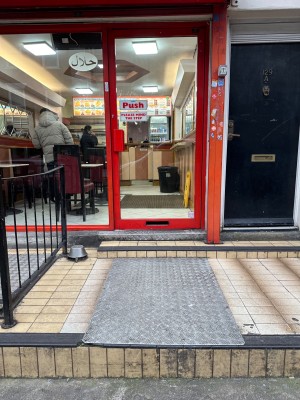 One step up to standing area followed by two more steps to the main entrance. Glass door with red doorframe. Push from left to open
