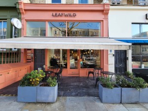 From street, facing venue. Planters on left and right. Outdoor seating behind. Path in centre to entrance.