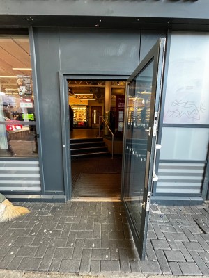 Glass door with grey frame. Pull silver handle on left to open. Doorbell on left of door.