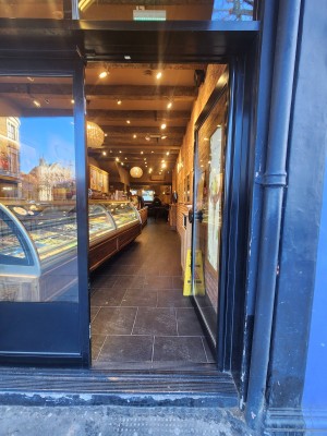 Glass door with black, metal frame. Push from left to open.