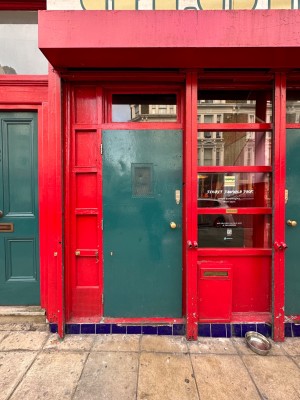 Green wooden door with red doorframe. Handle at right pull to open