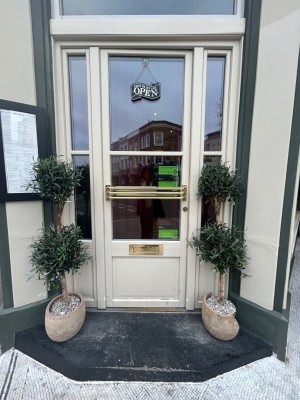 White door with glass panels. Push from right to open. Planters to left and right of door.