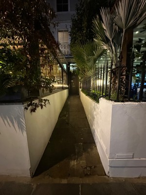 Looking ahead from pavement to alleyway leading to alternative entrance. Path veers right at end to entrance.