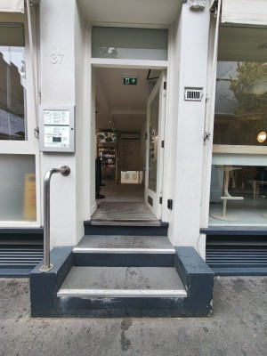 Three steps up to white framed glass door. Push silver handle on left to open. Silver handrail on left of steps.
