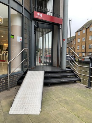 From street, facing venue. Three steps up to doorway. Silver handrails along both sides. Ramp up on left.