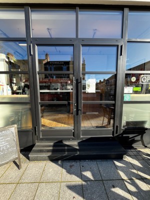 Glass double doors with black frame. Pull from black handles in centre to open.