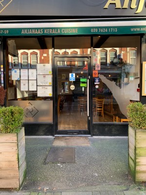 Potted plants to left and right, path down centre to entrance on back. Glass door with black frame ahead. Push door from right to open.