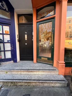 Two steps up to entrance on the right. Green framed glass door. Push golden handle on right to open.