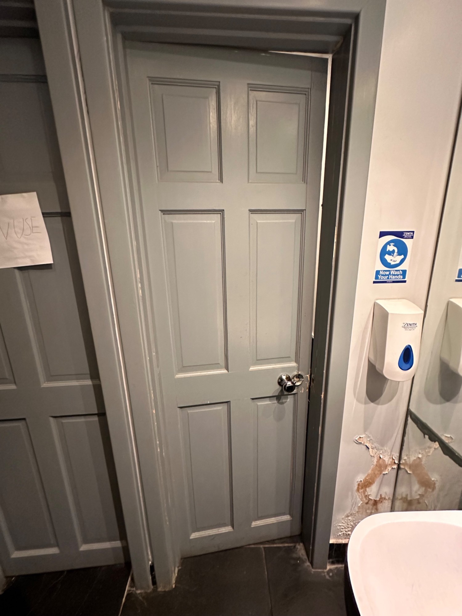 From right of door facing straight. Grey wooden door ahead. Push from handle on right to open.
