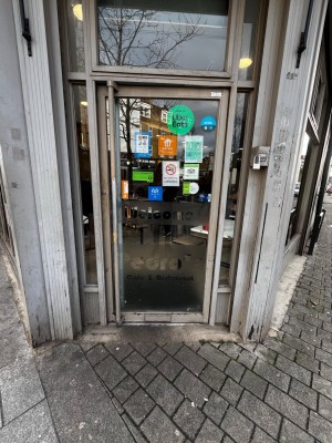Glass door with grey metal frame. Push from right to open.
