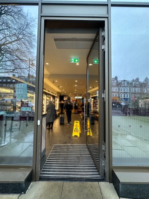 Glass door with brown metal frame. Push silver handle on left to open. Doorbell on left doorframe.