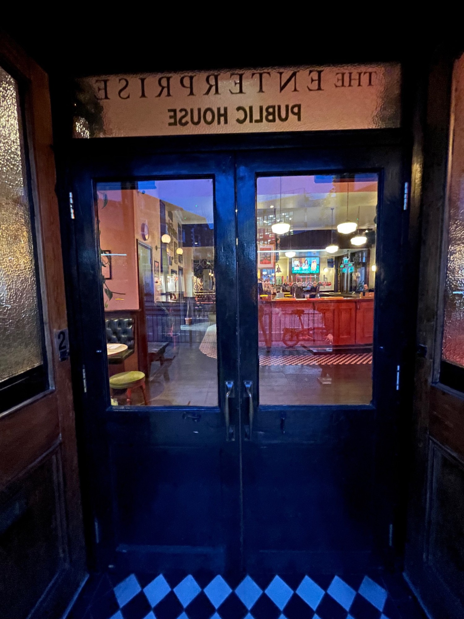 From doorway, facing straight. Glass door with black, wooden frame ahead. Pull metal handles in middle to open.