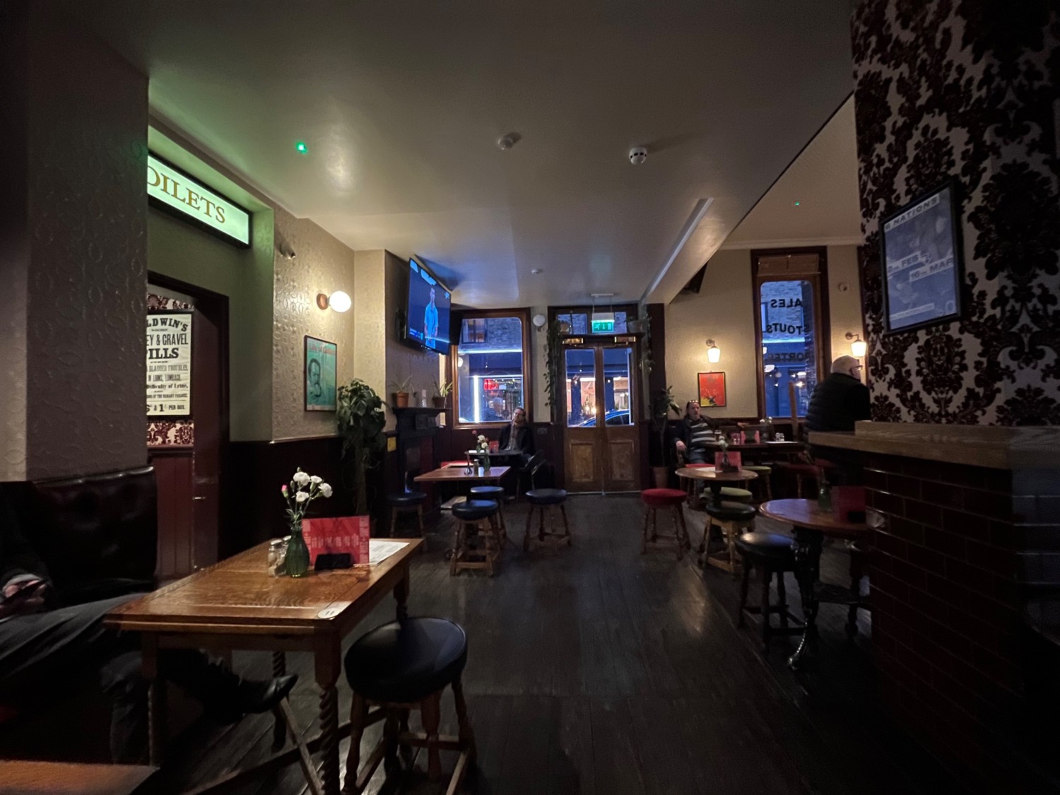 From back half-booths and stools, facing right. Half-booths along left and back. Archway to bathroom in between. Tables and stools along right.