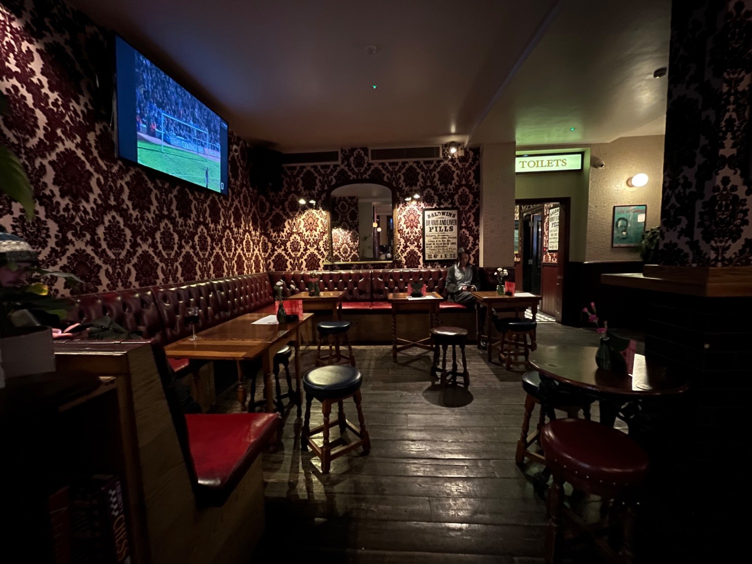 From end of path, facing straight. Half-booths, table and stools along left and back. Archway at bathroom at back right.