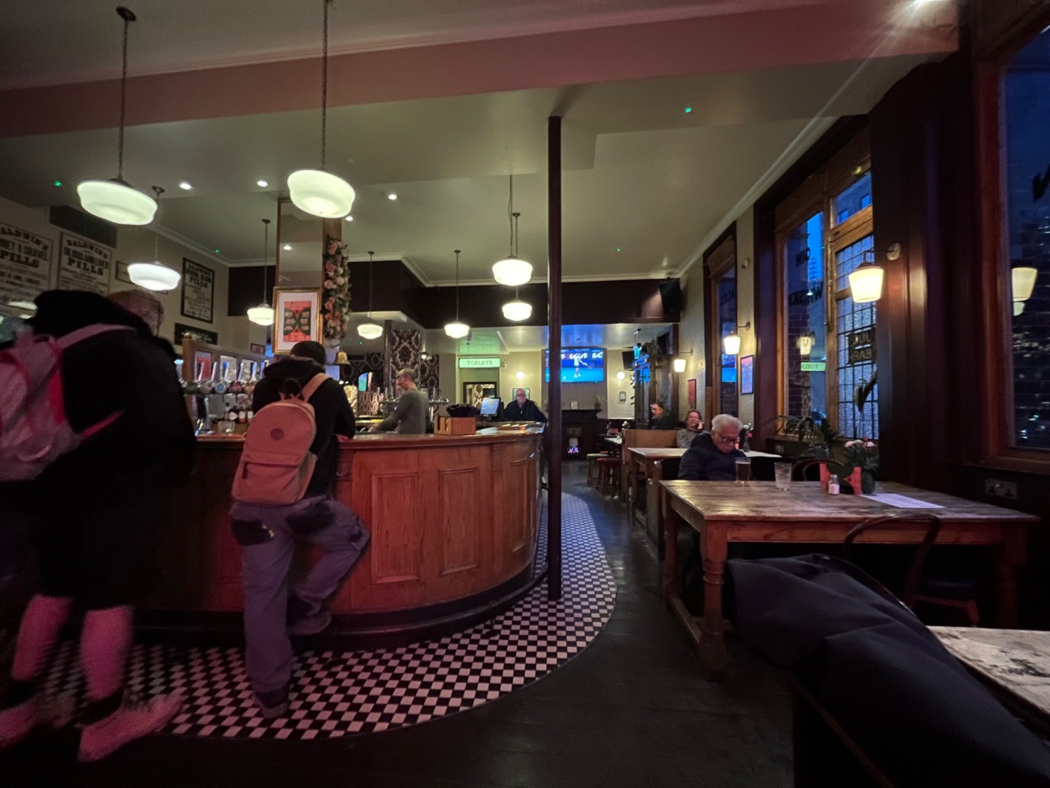 From tables and benches, facing left. Bar counter at back left. Pillar to its right. Tables, benches and chairs along right.