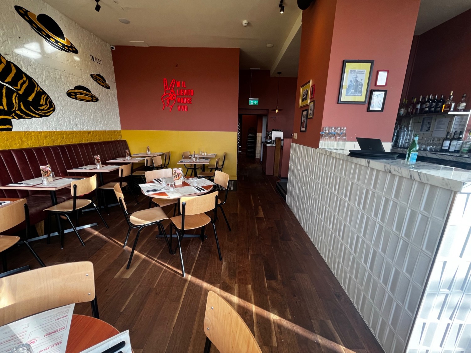 Facing right from tables and chairs. Tables with chairs to left. Half booths along left wall. Path to bathroom ahead.