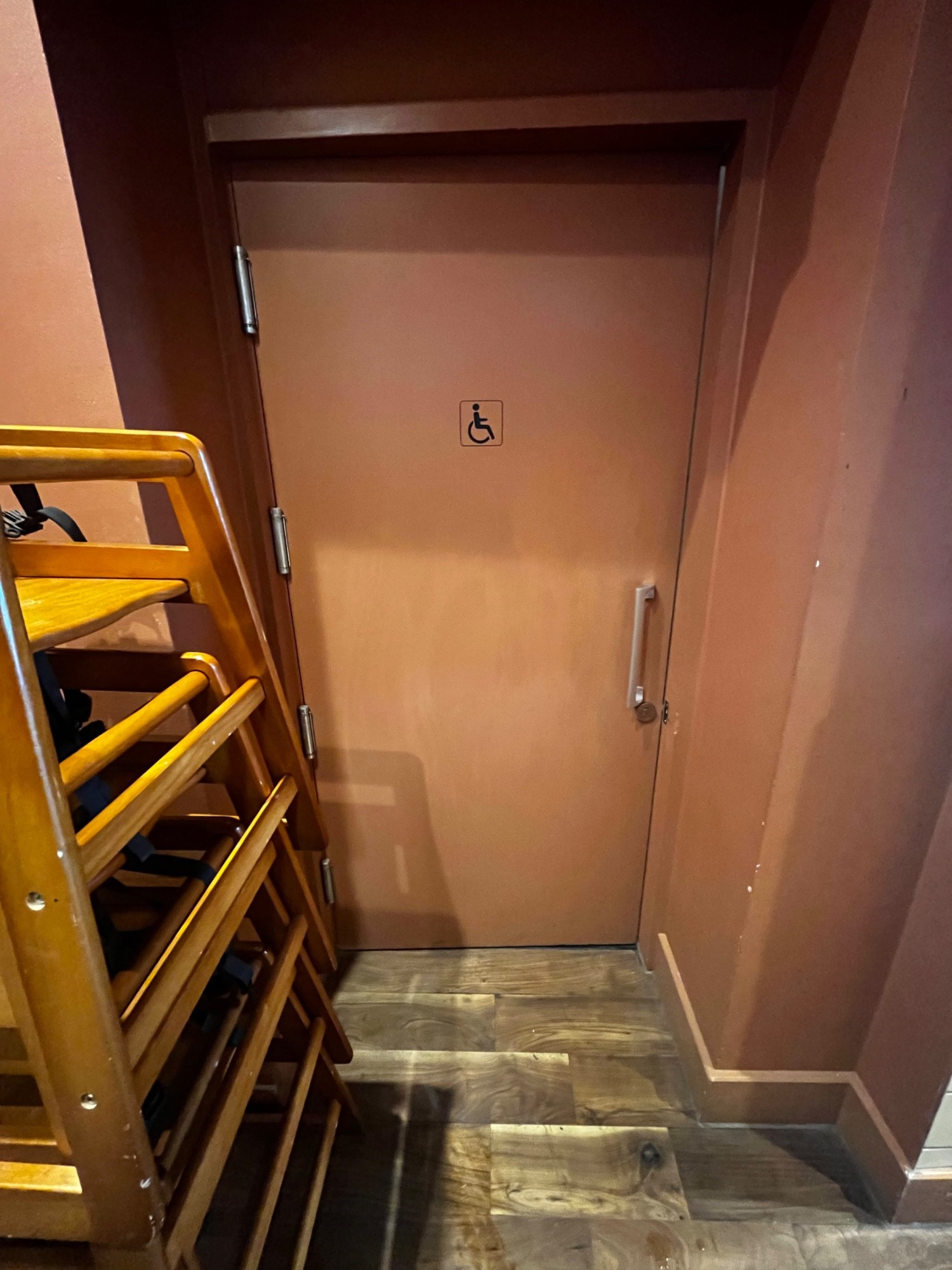Pale pink wooden bathroom door facing right from archway. Push from right to open. Baby chairs on left of door.