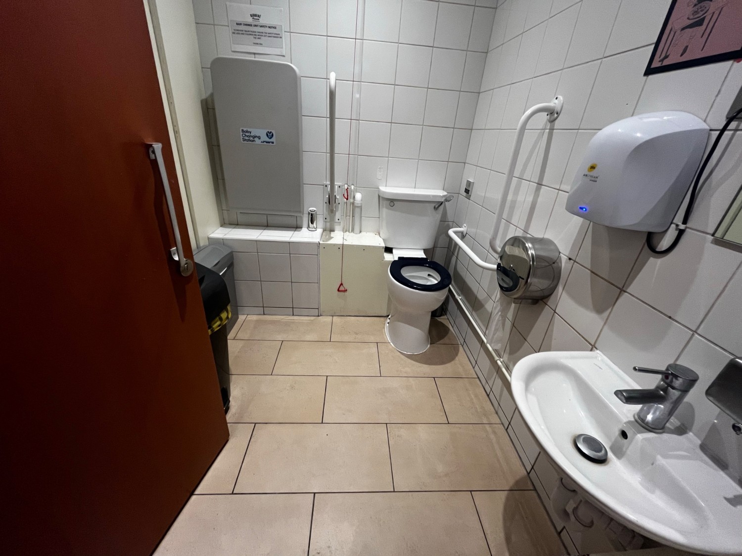 From door facing straight. Sink on right. Toilet on wall ahead. Pull cord on left of toilet. Baby change on wall ahead to left of toilet.