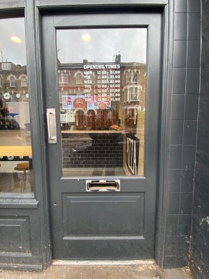Glass door with black, wooden door ahead. Push silver handle on left to open.
