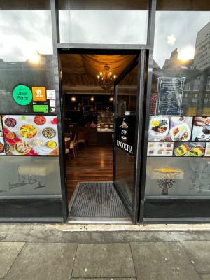 Glass door with black metal frame. Push from left to open.