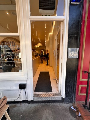 Glass door with white, wooden frame ahead. Push silver handle on left to open.