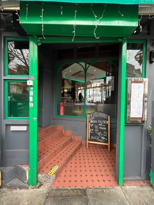 Preceding open archway with green border. Steps on left lead to main door.
