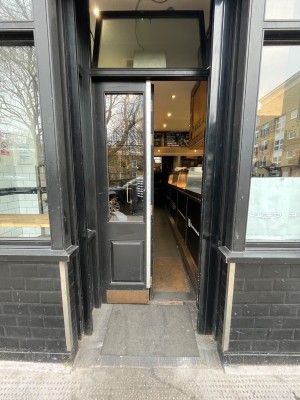Built in ramp leading to black wooden door with glass panels. Push right side of door from right to open. Door slides open wider to left.