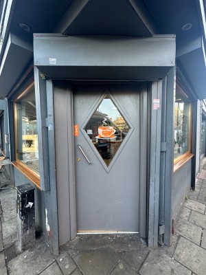 Wooden glass paneled door with grey doorframe. Handle at left. Push to open
