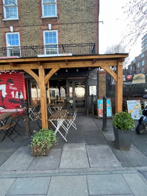 From street facing main entrance. Walkway under wooden archway leads to door directly ahead.