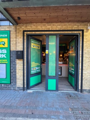 Two single green doors outlined in black and divided by large pillar. Push door on left from right to enter. Push door on right from left to enter.