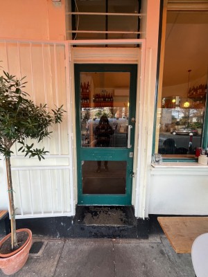 White metal gate door. Pull on right to open. Glass door within green frame immediately after. Pull handle to open.