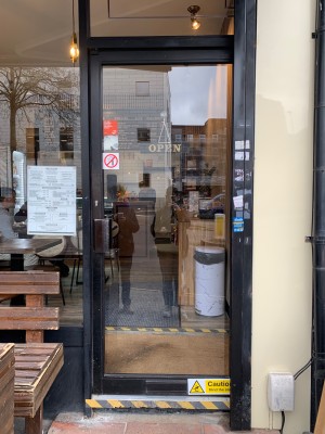 Glass door with black frame. Push handle on left to open.